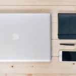 Lukket MacBook ved siden af en notesbog, pen og smartphone på et træbord