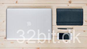 Lukket MacBook ved siden af en notesbog, pen og smartphone på et træbord